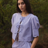Woman wearing a blue striped outfit standing outdoors with greenery in the background