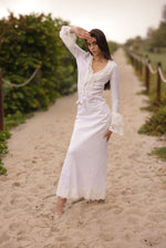 Woman in a white dress standing on a sandy path with greenery around.