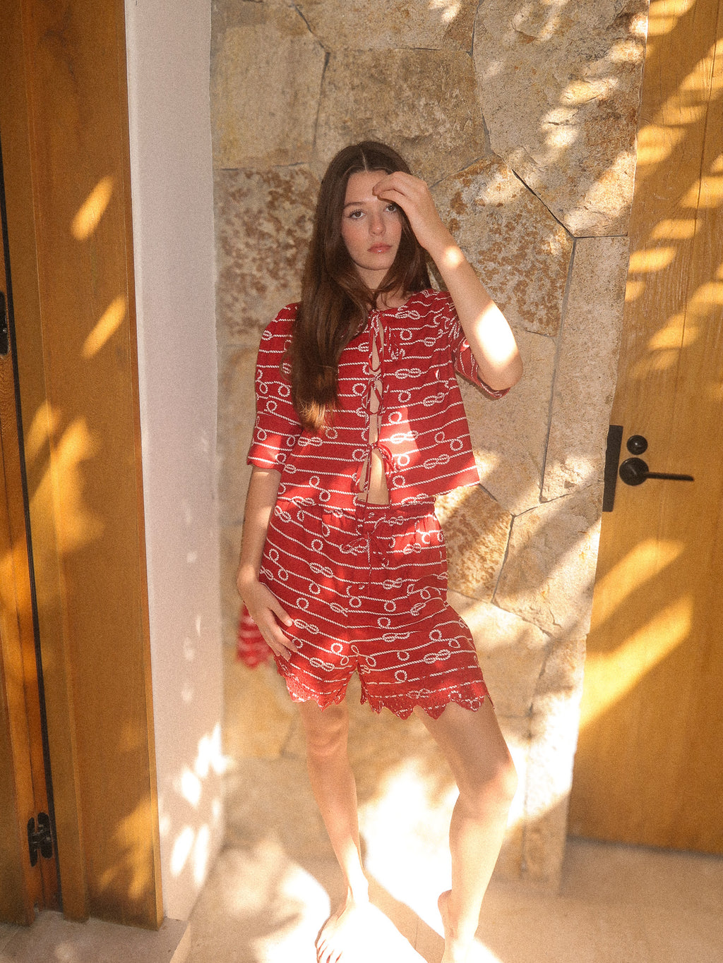 Woman wearing a red outfit with a pattern in a sunlit room.
