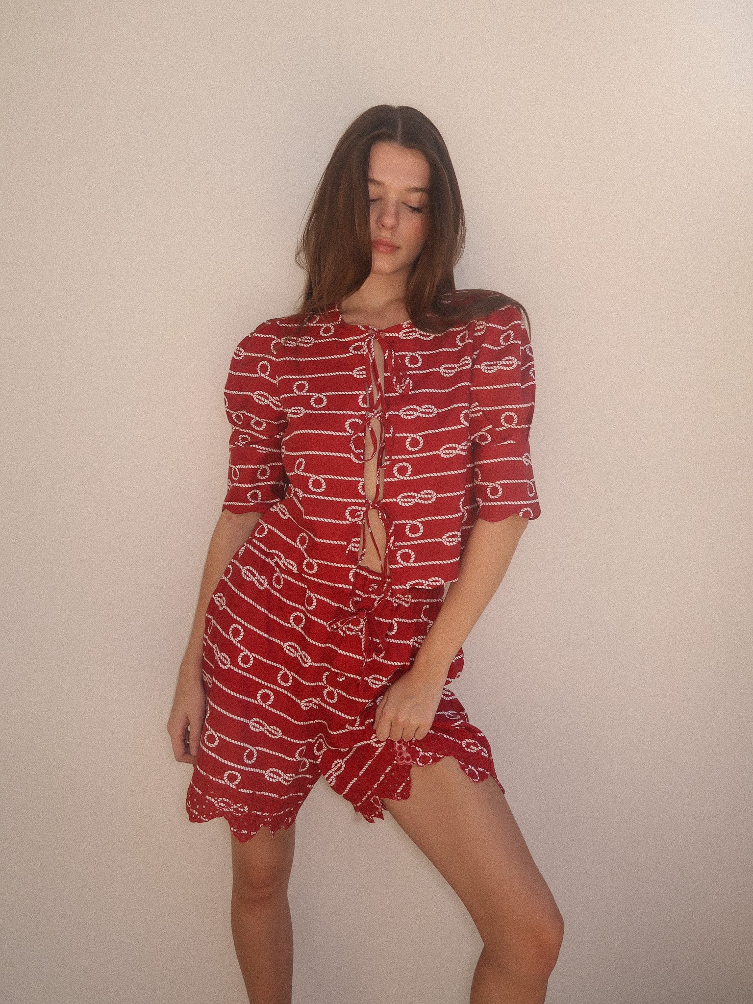 Woman wearing a red dress with white patterns against a plain background