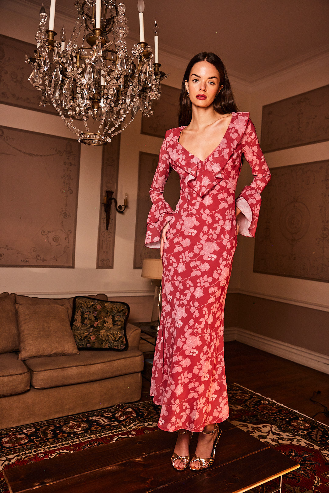 Woman in a red floral dress standing in a room with a chandelier and sofa.