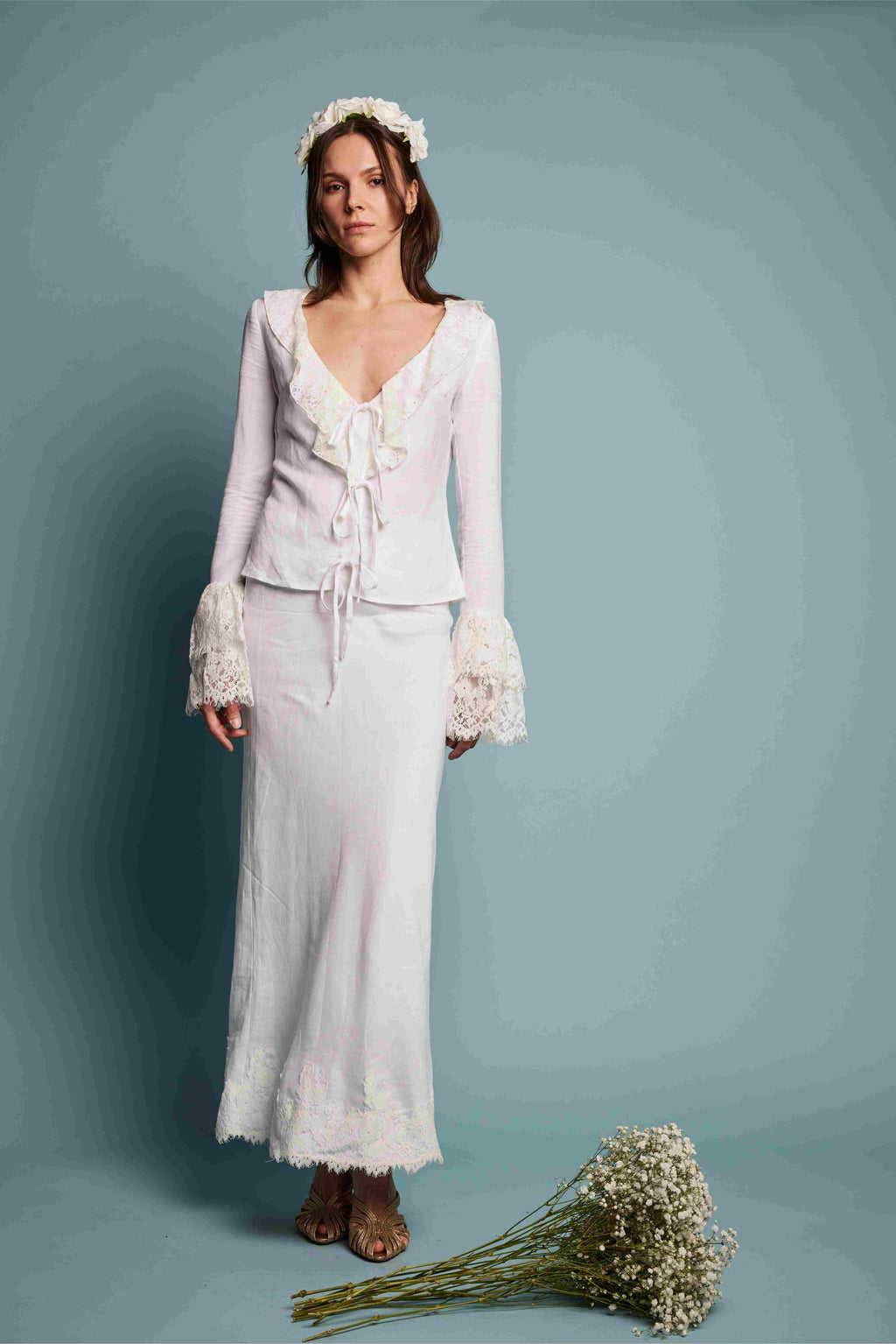 Woman in a white bridal outfit with a floral headpiece and bouquet on a blue background