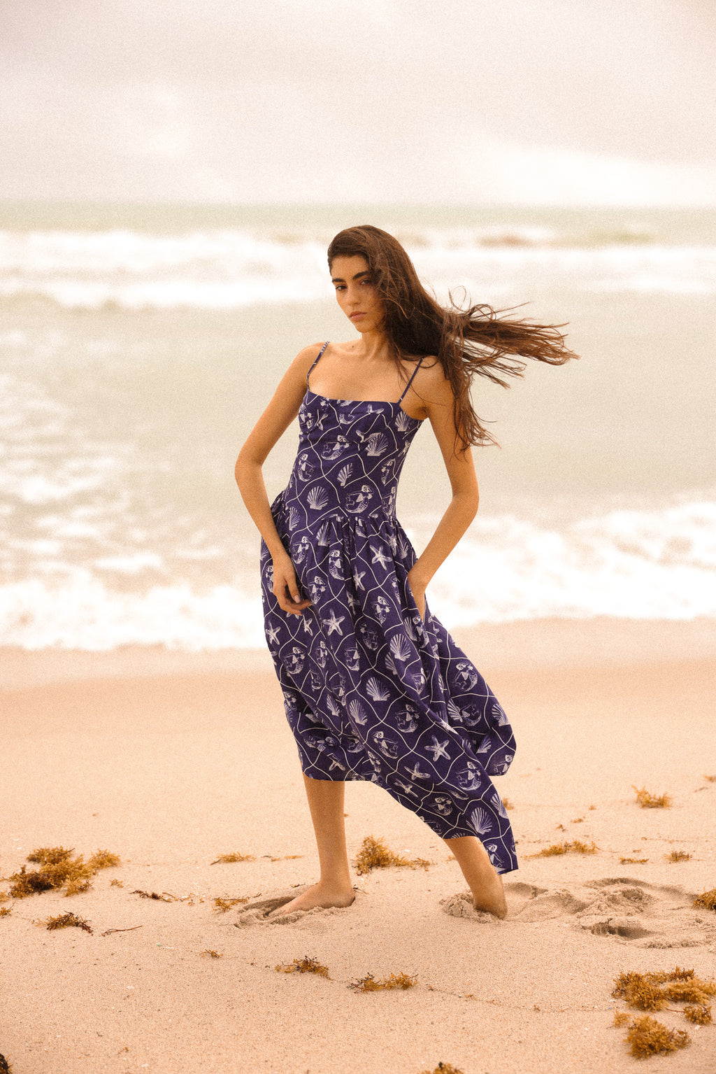 Woman in a purple dress standing on a beach with waves in the background