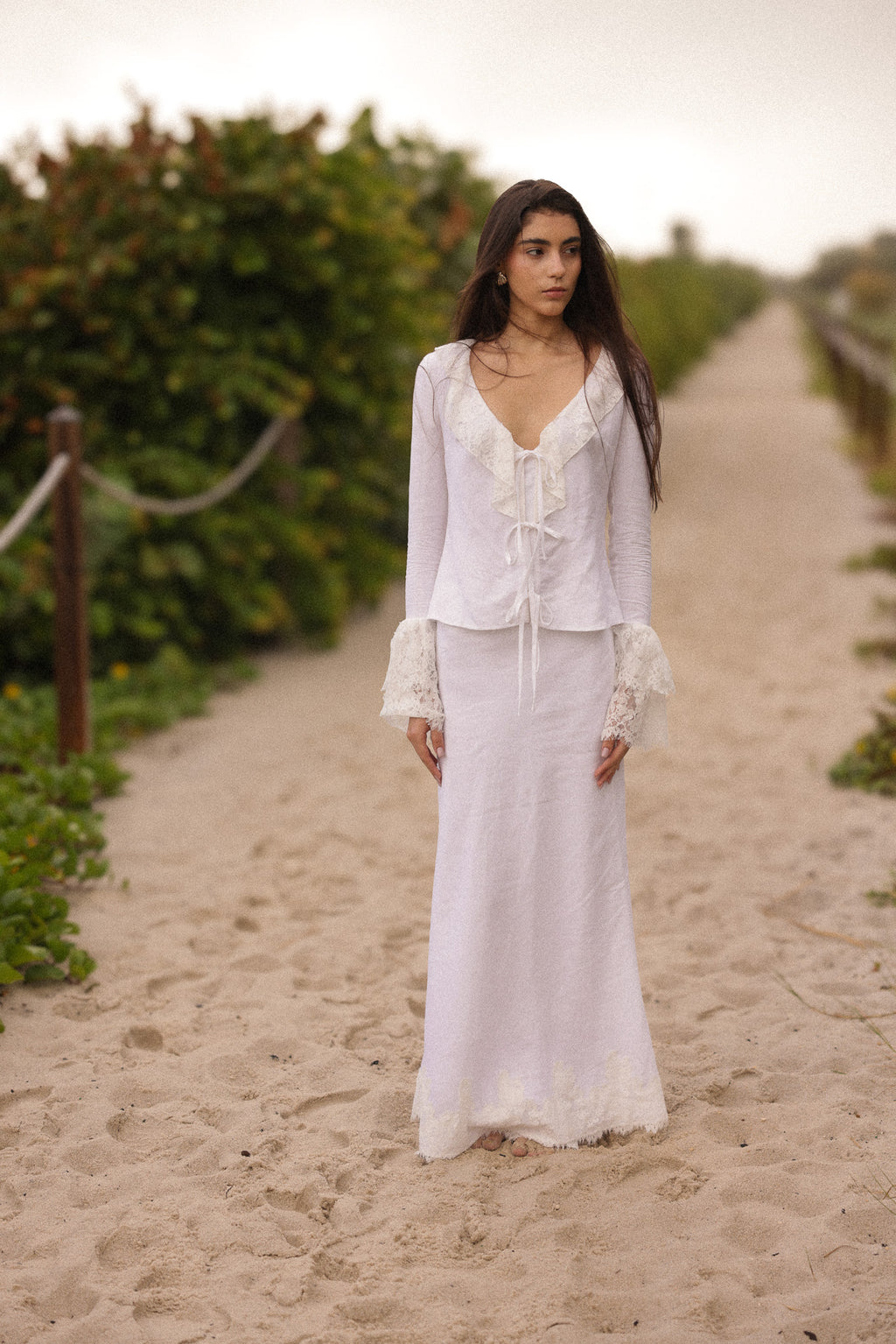 Model wearing a white linen lace tie-front top with matching maxi skirt, styled for a romantic coastal summer look by Sister New York