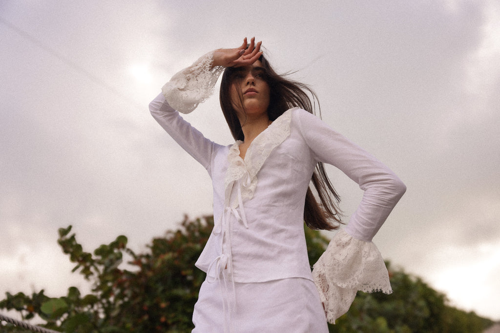  Model wearing a white linen tie-front top with lace bell sleeves, styled for an elevated summer resort look by Sister New York.